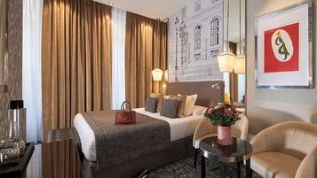 A hotel room with a large bed, a desk, a chair, a lamp, and a framed artwork on the wall.