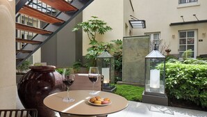 A round table with a plate of macarons and two wine glasses, a large ceramic vase, and a staircase with wooden beams. - Hôtel La Lanterne & Spa By Timhotel (Paris)