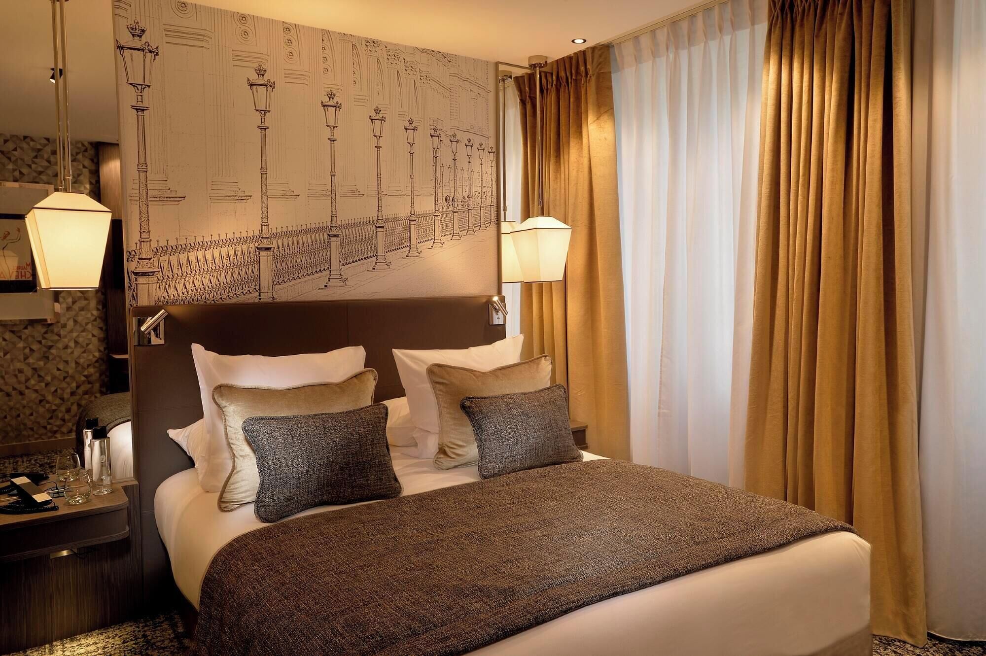 A hotel room with a large bed, two bedside lamps, a headboard with a cityscape mural, and a window with curtains.