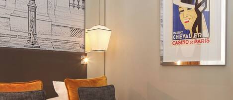 A hotel room with a bed, a lamp, a framed poster, and a wall with a drawing.