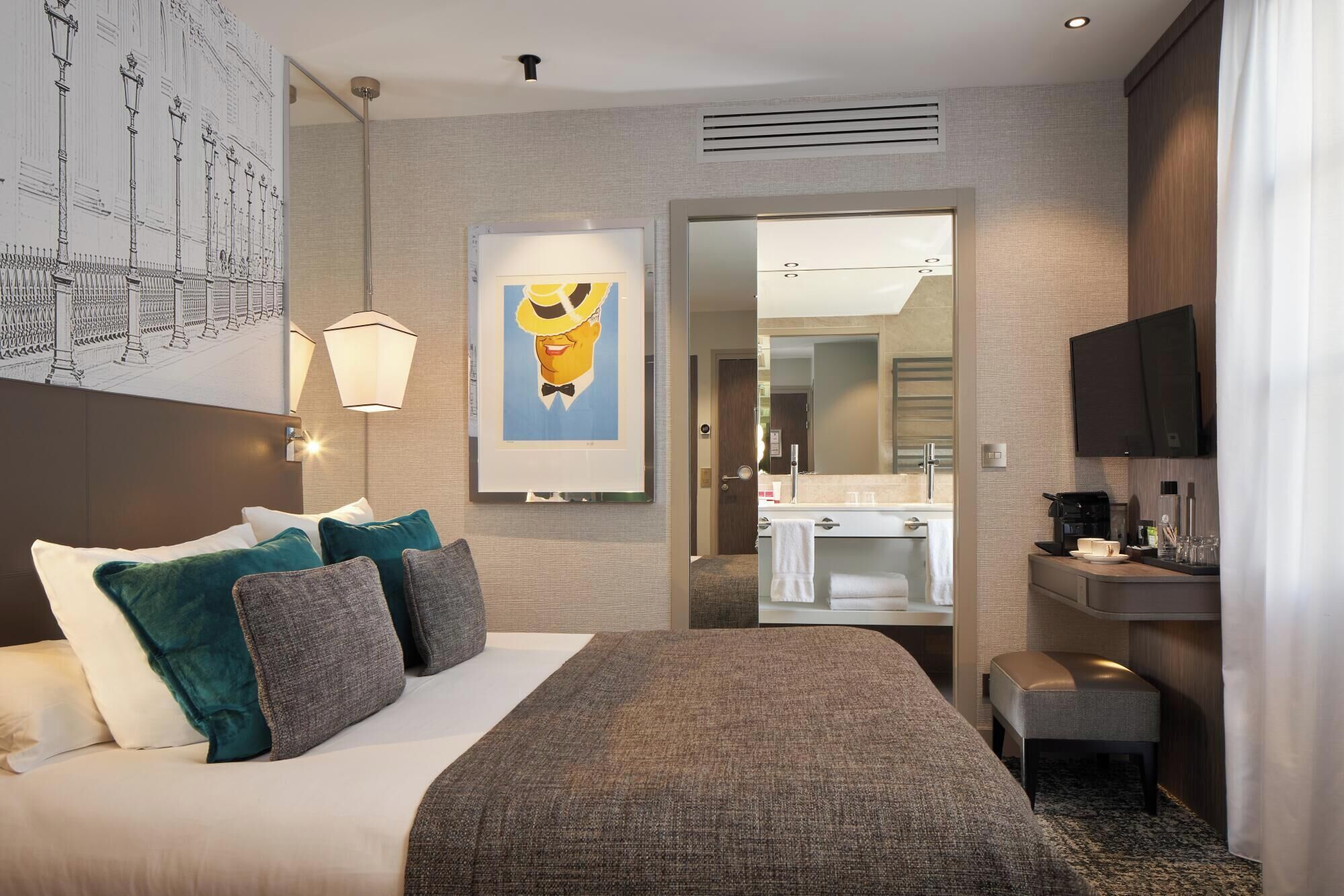 Habitación de hotel con cama, escritorio, televisor y baño visible a través de una puerta abierta.