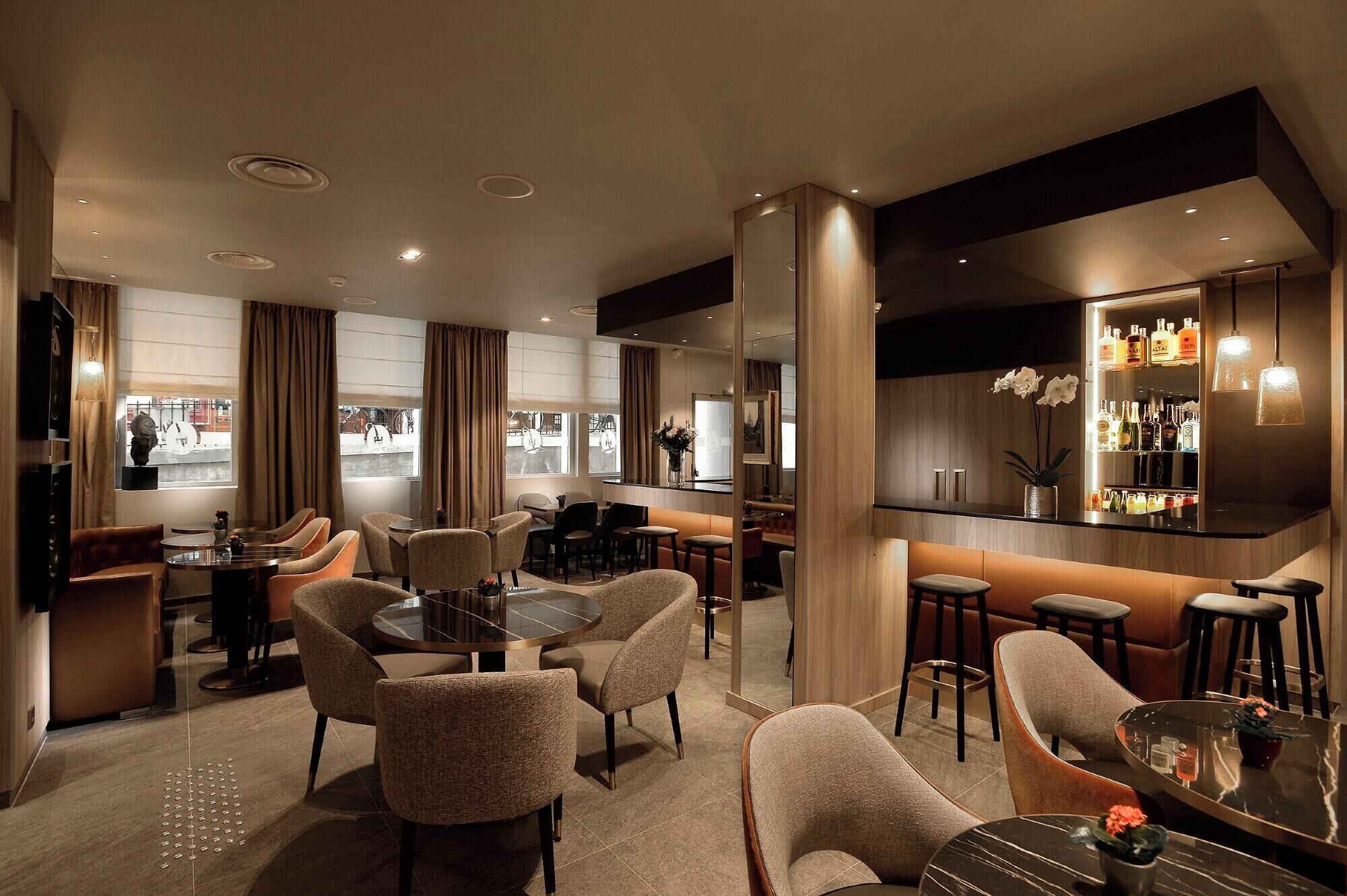 Un hall d’hôtel moderne doté d’un bar, de différents espaces de détente et de grandes fenêtres offrant une vue panoramique.