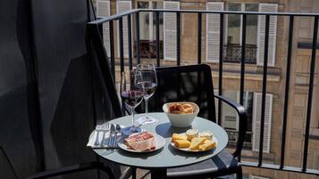 A balcony table with a meal setup including plates of food, glasses of wine, and a bowl of pastries.
