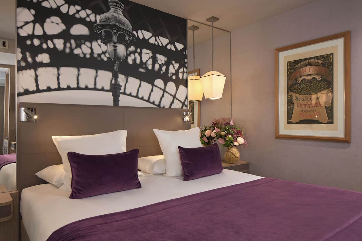 A hotel room with a large bed, a nightstand, a vase of flowers, and a framed picture on the wall.