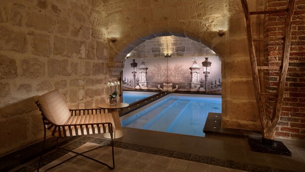 A stone-walled room with a pool, a wooden chair, and a ladder. - Hôtel La Lanterne & Spa By Timhotel (Paris)
