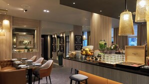 A modern bar area with seating, a counter with food and drink items, and framed artwork on the walls. - Hôtel La Lanterne & Spa By Timhotel (Paris)