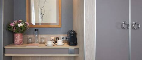 A modern bathroom with a wooden vanity, a framed artwork, a vase of flowers, and a coffee maker.