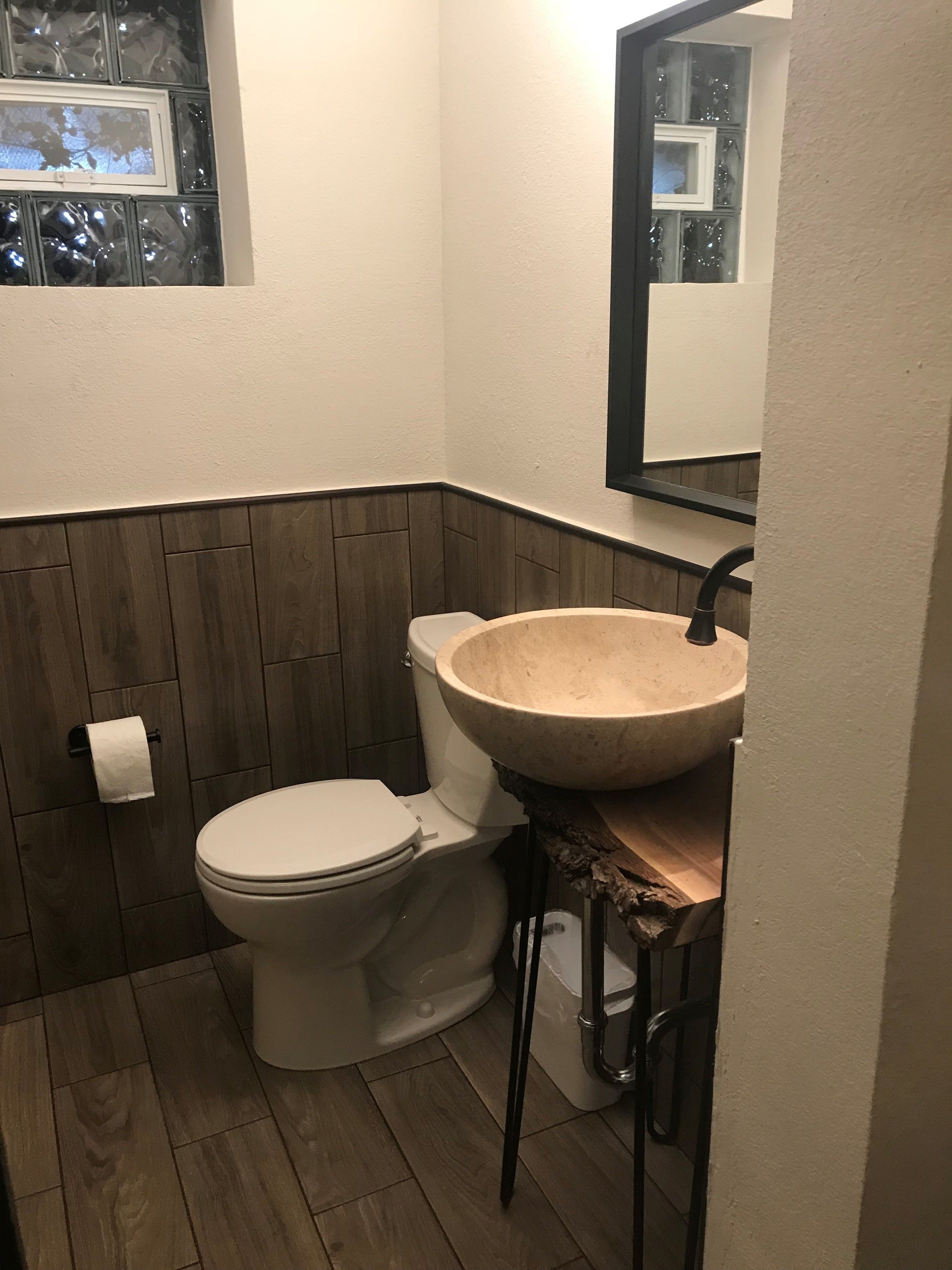A bathroom with a wooden floor, a white toilet, a large beige sink, and a mirror above the sink.