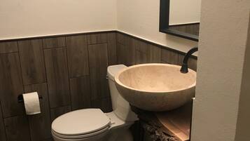 A bathroom with a wooden floor, a white toilet, a large beige sink, and a mirror above the sink.