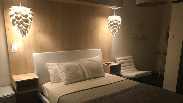 Een moderne slaapkamer met een groot bed, twee nachtkastjes, een stoel en een bijzondere hanglamp.