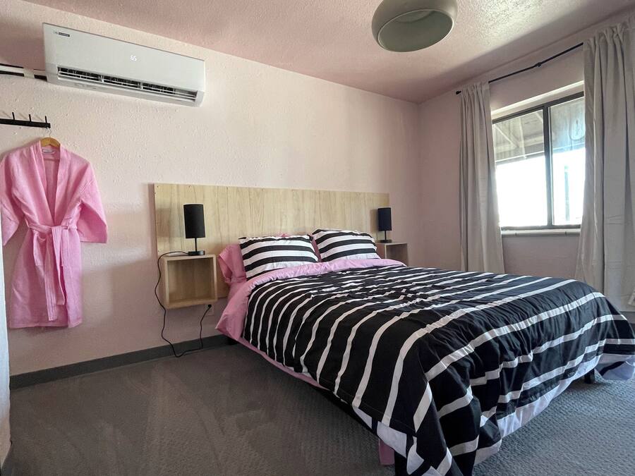 A hotel room with a bed, a bedside table with a lamp, a hanging robe, and an air conditioning unit.