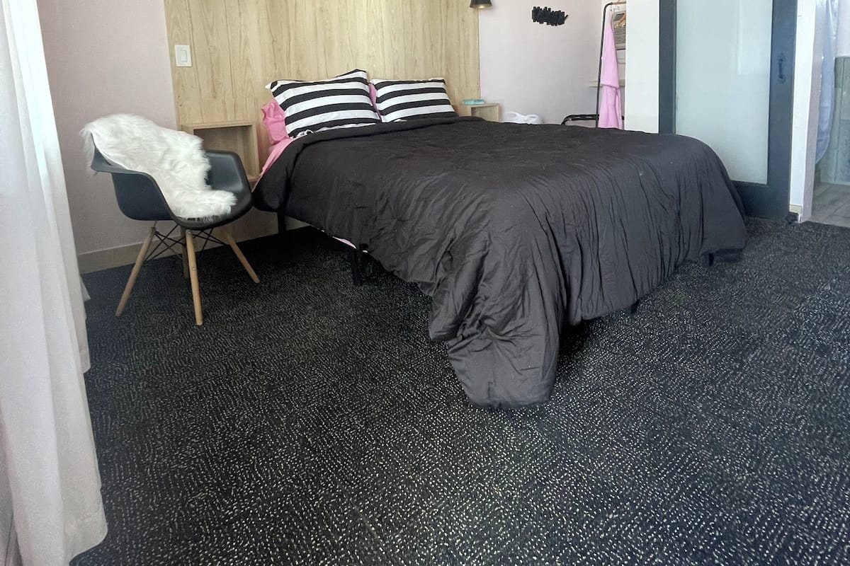 A modern bedroom with a bed, a chair, a desk, and a large window.