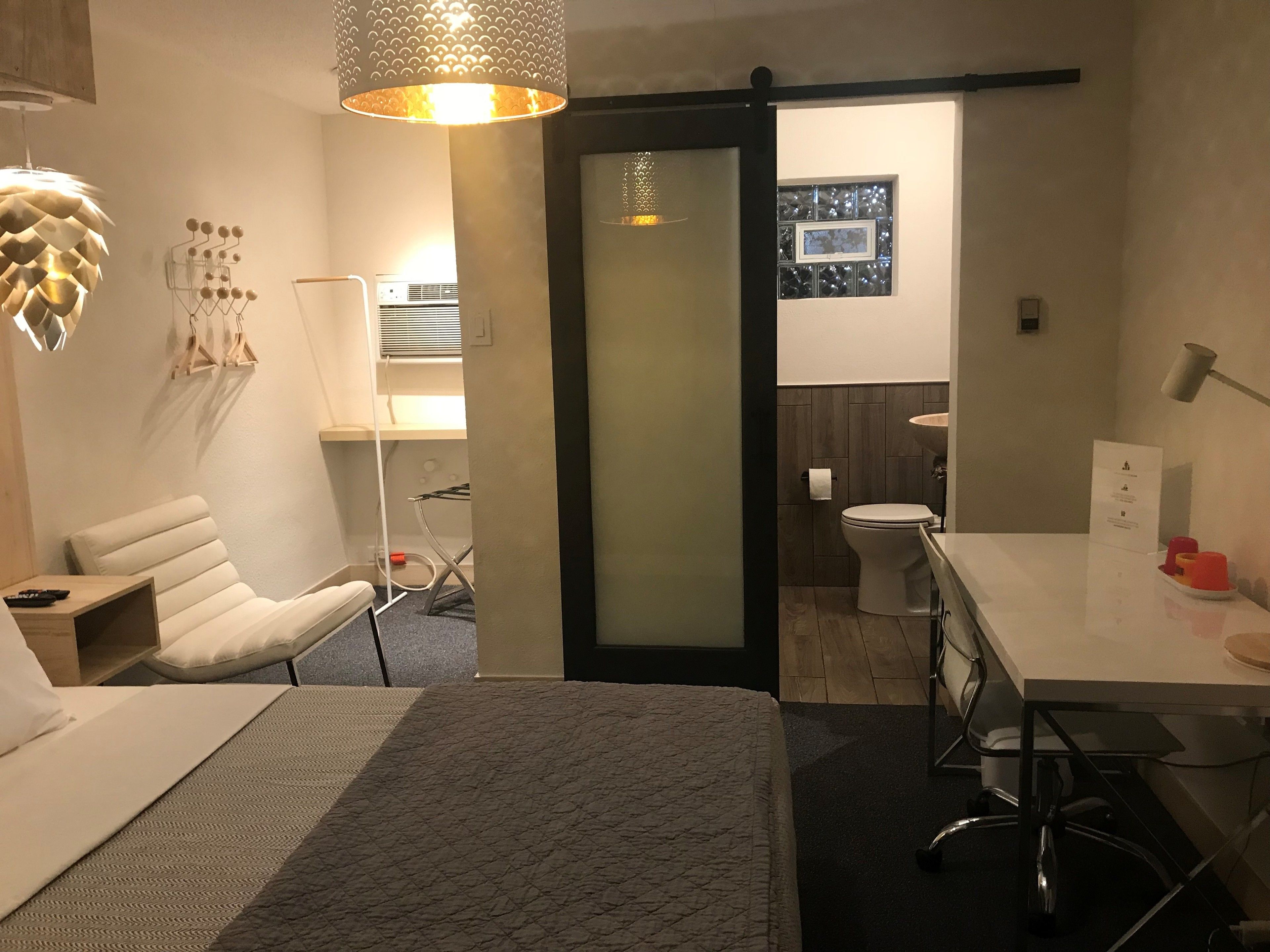 A modern hotel room with a bed, a desk, a chair, a bathroom, and a sliding door.