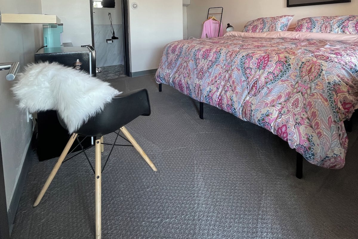 A bedroom with a bed, a chair, a desk, a mirror, and a door.