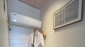 Een wasruimte met een droogrek, een witte wasmand en een witte badjas hangend aan een houten kapstok.