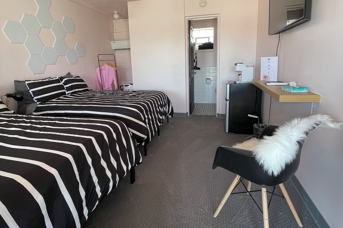 A hotel room with two beds, a desk, a chair, a TV, and a mirror.