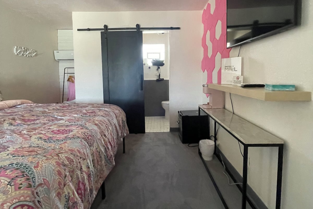 A bedroom with a bed, a desk, a TV, and a bathroom visible through an open door.