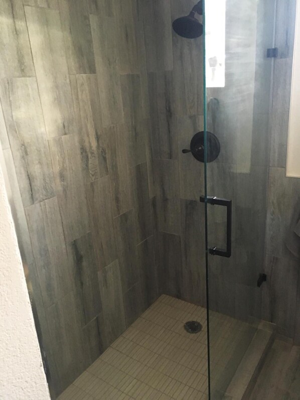 A glass-enclosed shower with a tiled floor and a wooden wall.