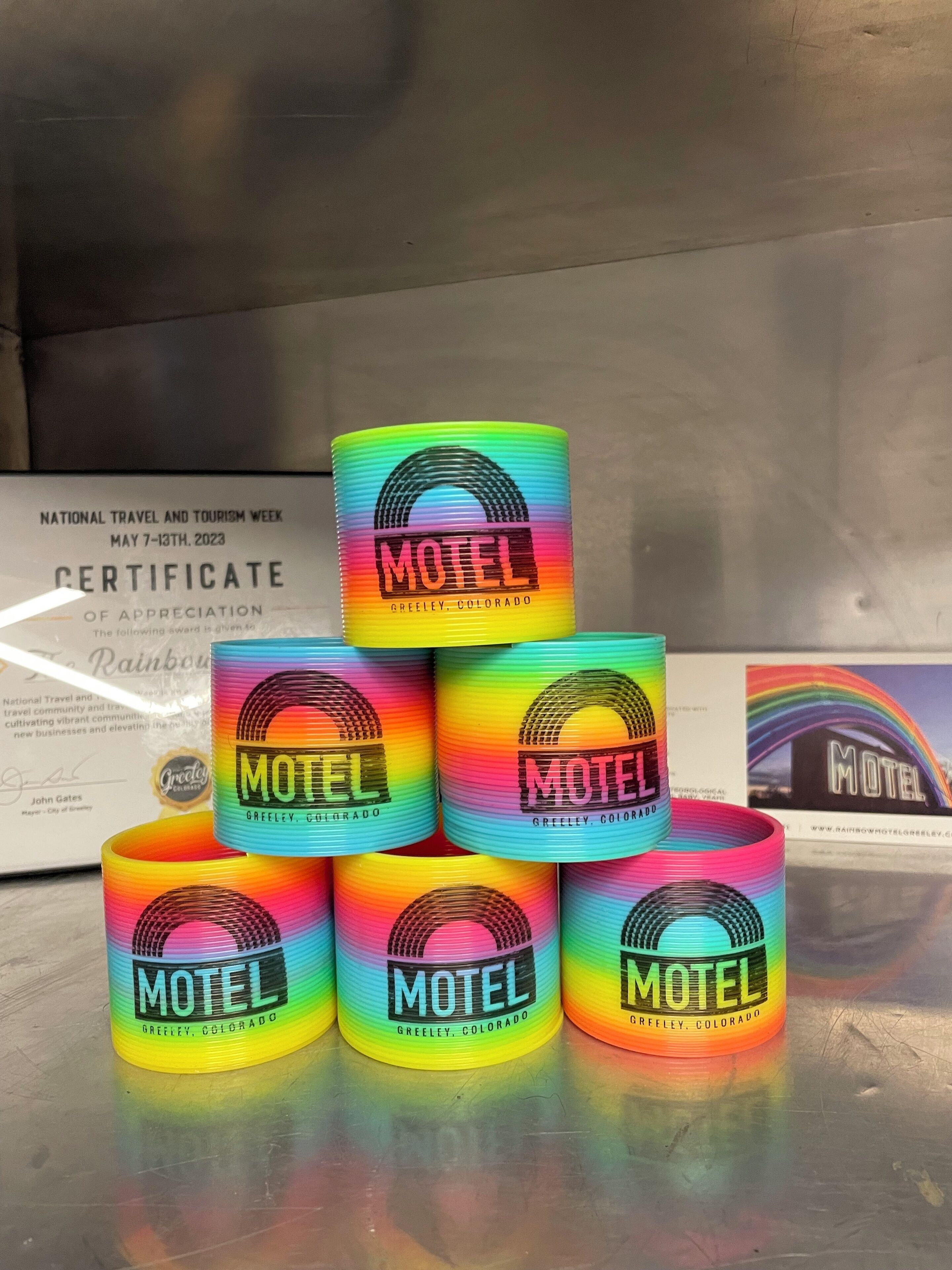 A stack of colorful cylindrical objects labeled 'Motel' with a certificate in the background.
