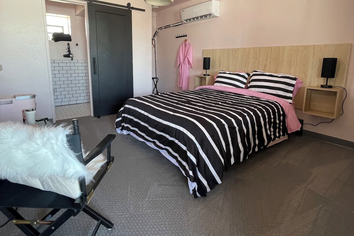A modern bedroom with a bed, a desk, a chair, a robe, and an air conditioning unit.