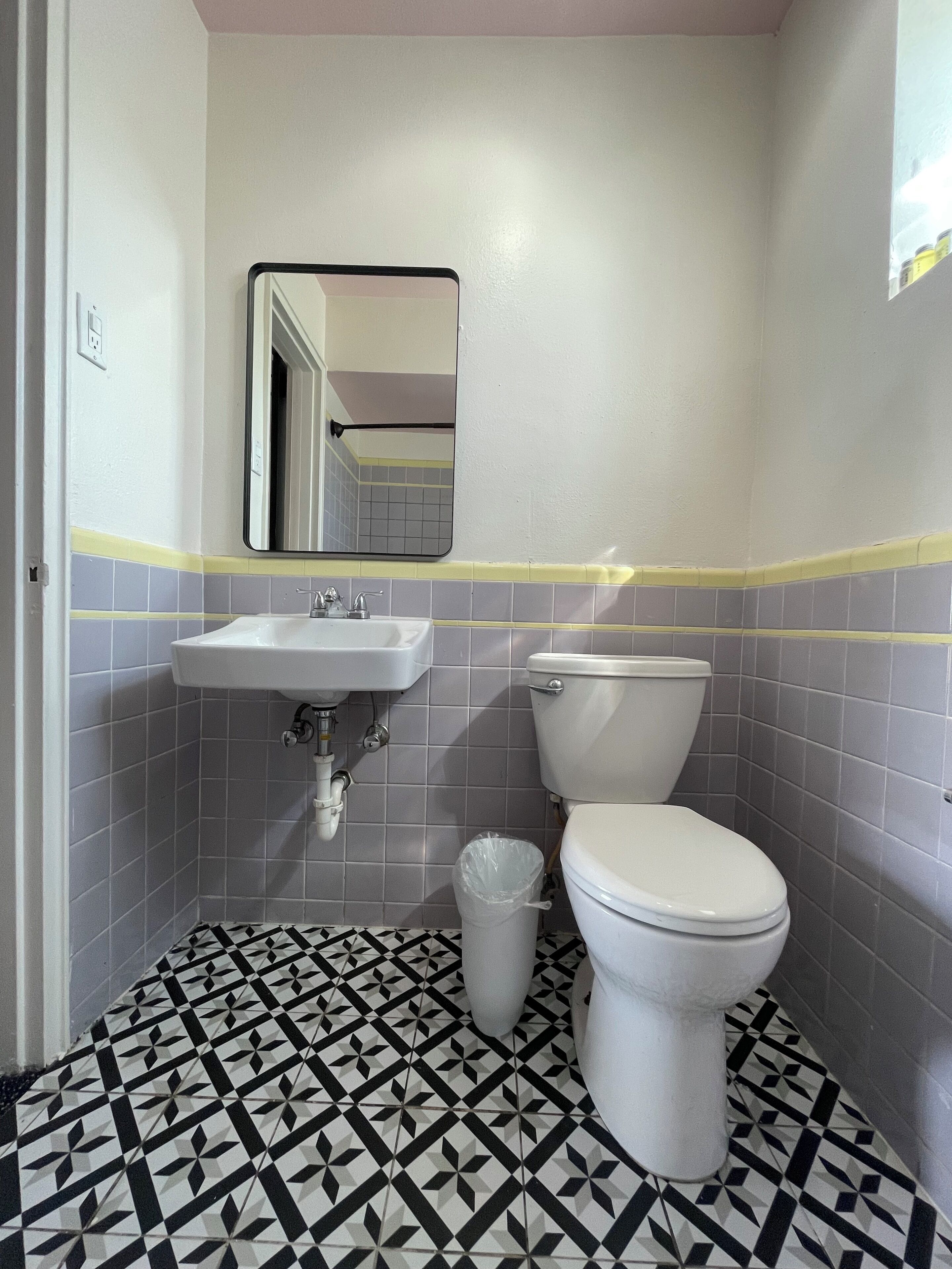 Een badkamer met een wit wastafel, toilet en een prullenbak. De vloer heeft een zwart-wit geometrisch tegelpatroon.