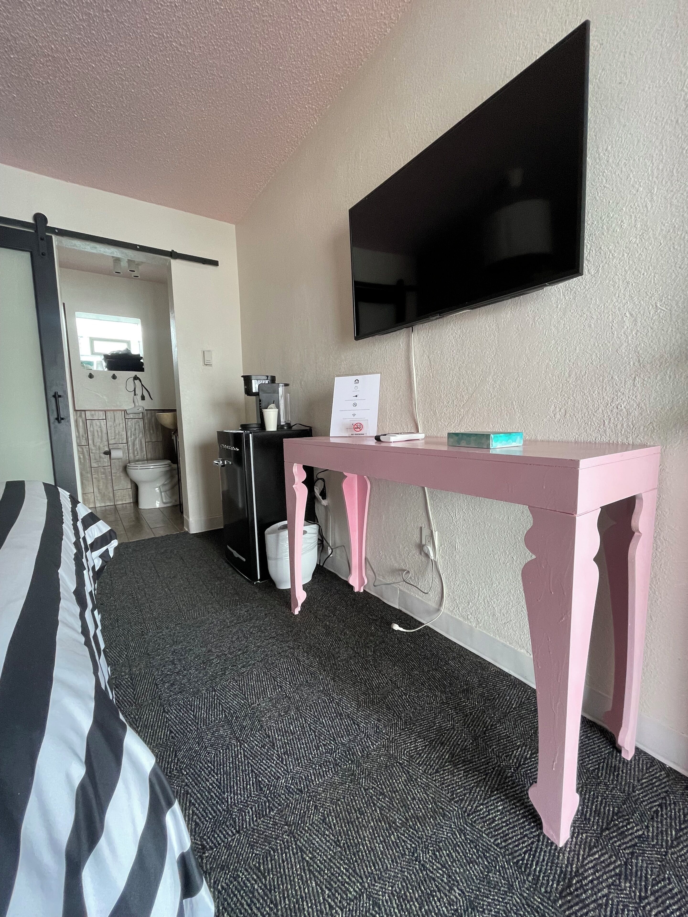 A hotel room with a bed, a desk, a television, a coffee machine, and a bathroom visible through an open door.