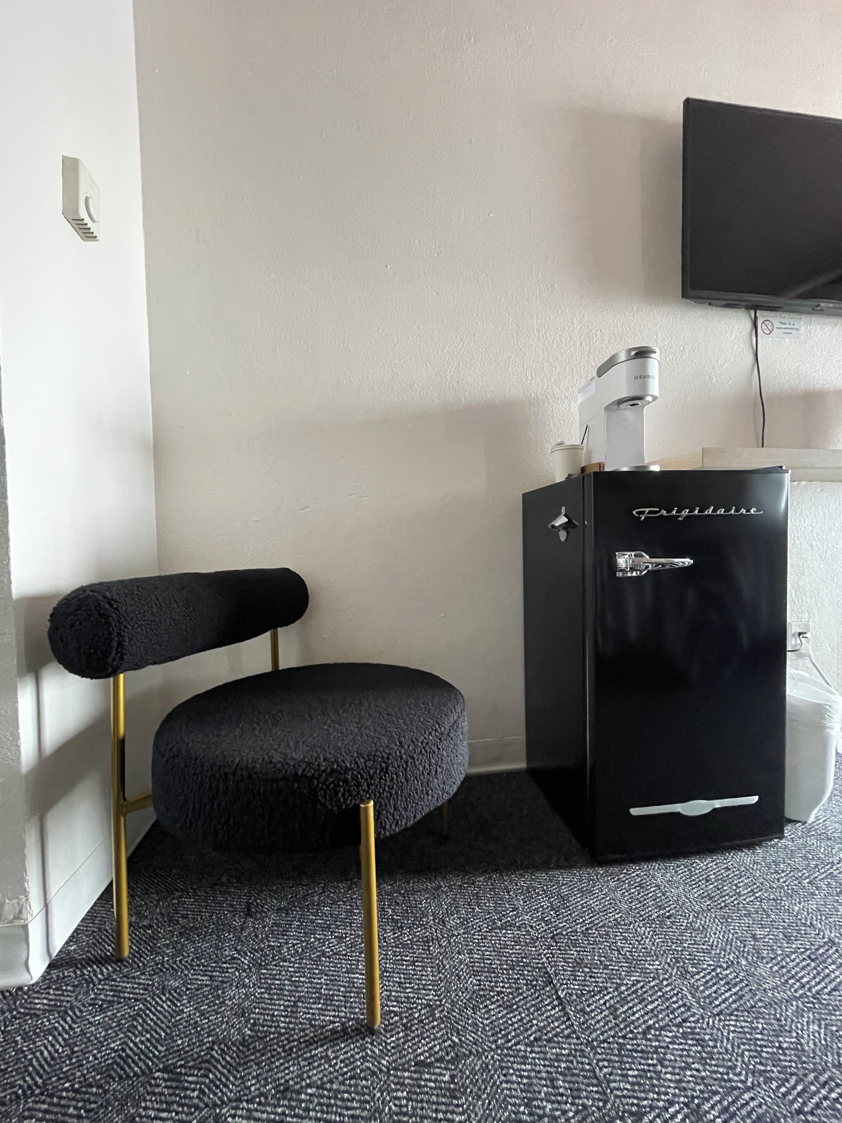 A compact room with a black upholstered chair, a black minibar, and a mounted television on the wall.