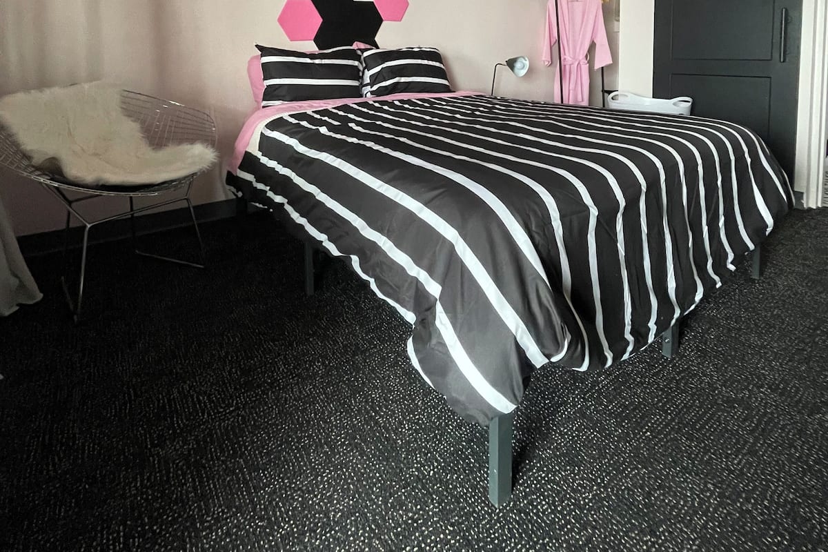 A bedroom with a black and white striped bedspread, a hexagonal wall decoration, a white chair, and a black door.