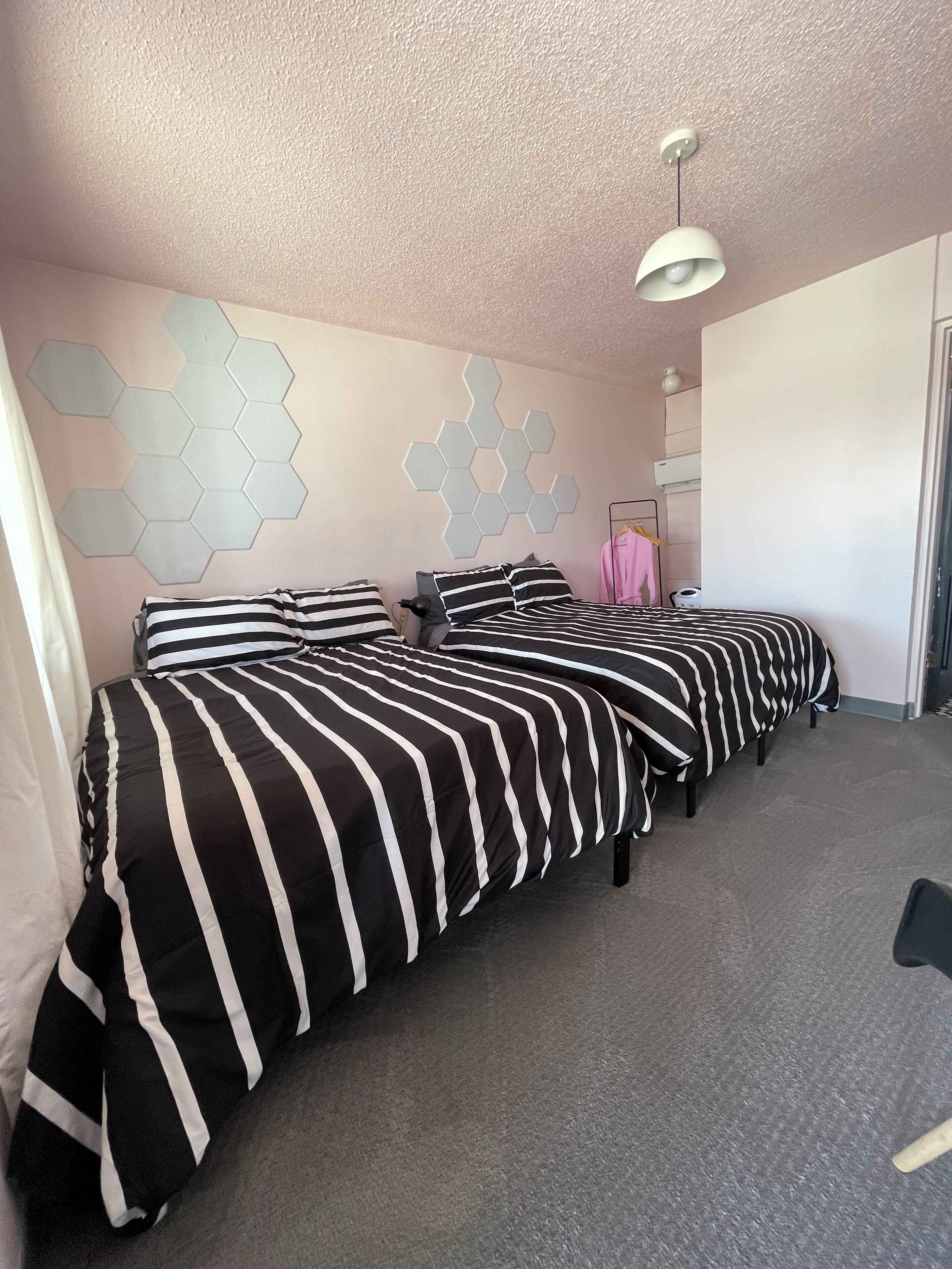 Habitación de hotel con dos camas, un adorno mural hexagonal, una lámpara de techo y un armario.