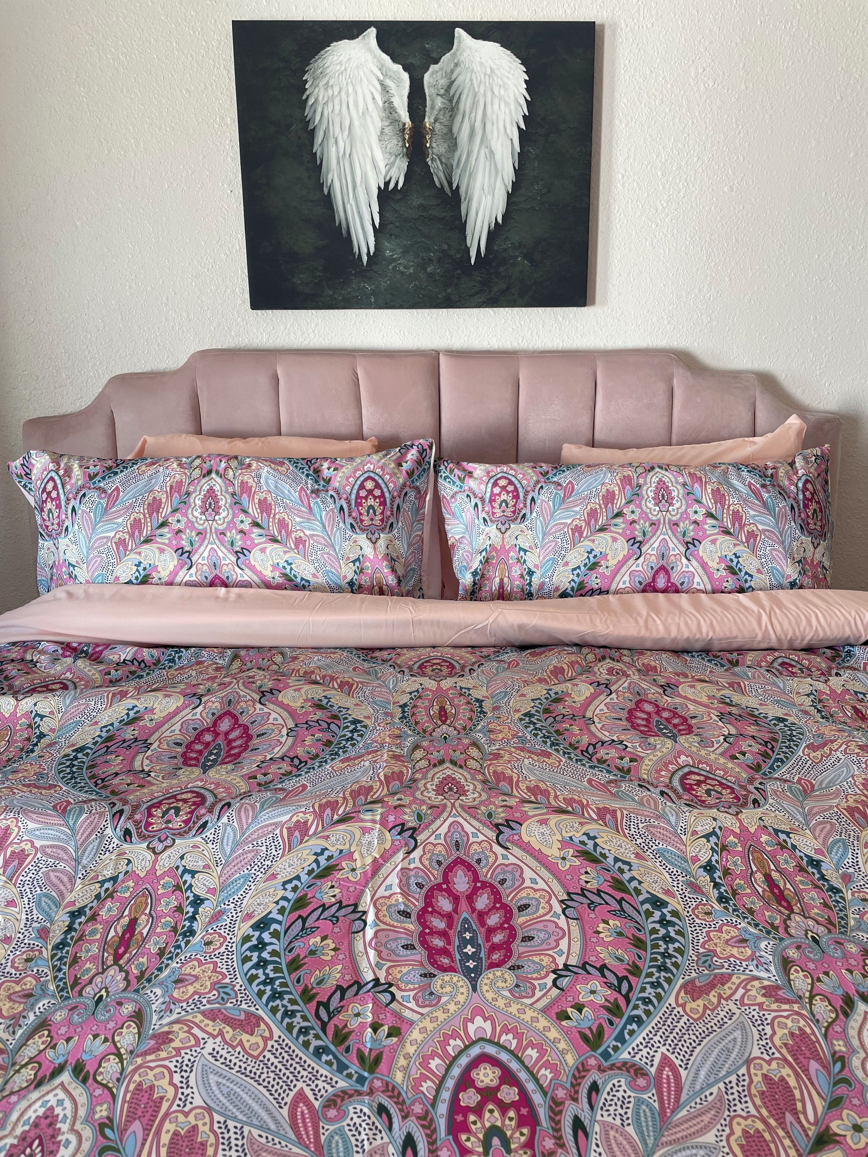 Una cama con colcha y almohadas a juego, un cabecero y una obra de arte en la pared con forma de alas de ángel blancas.