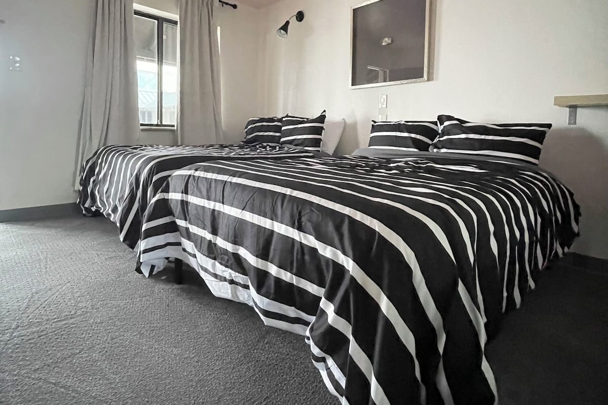 A room with a bed, a window with curtains, a wall-mounted lamp, and a mirror.