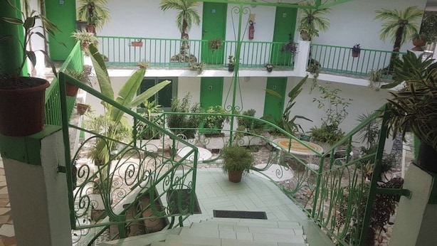 Un atrio de varios niveles con barandillas verdes, plantas en macetas y suelo de baldosas.