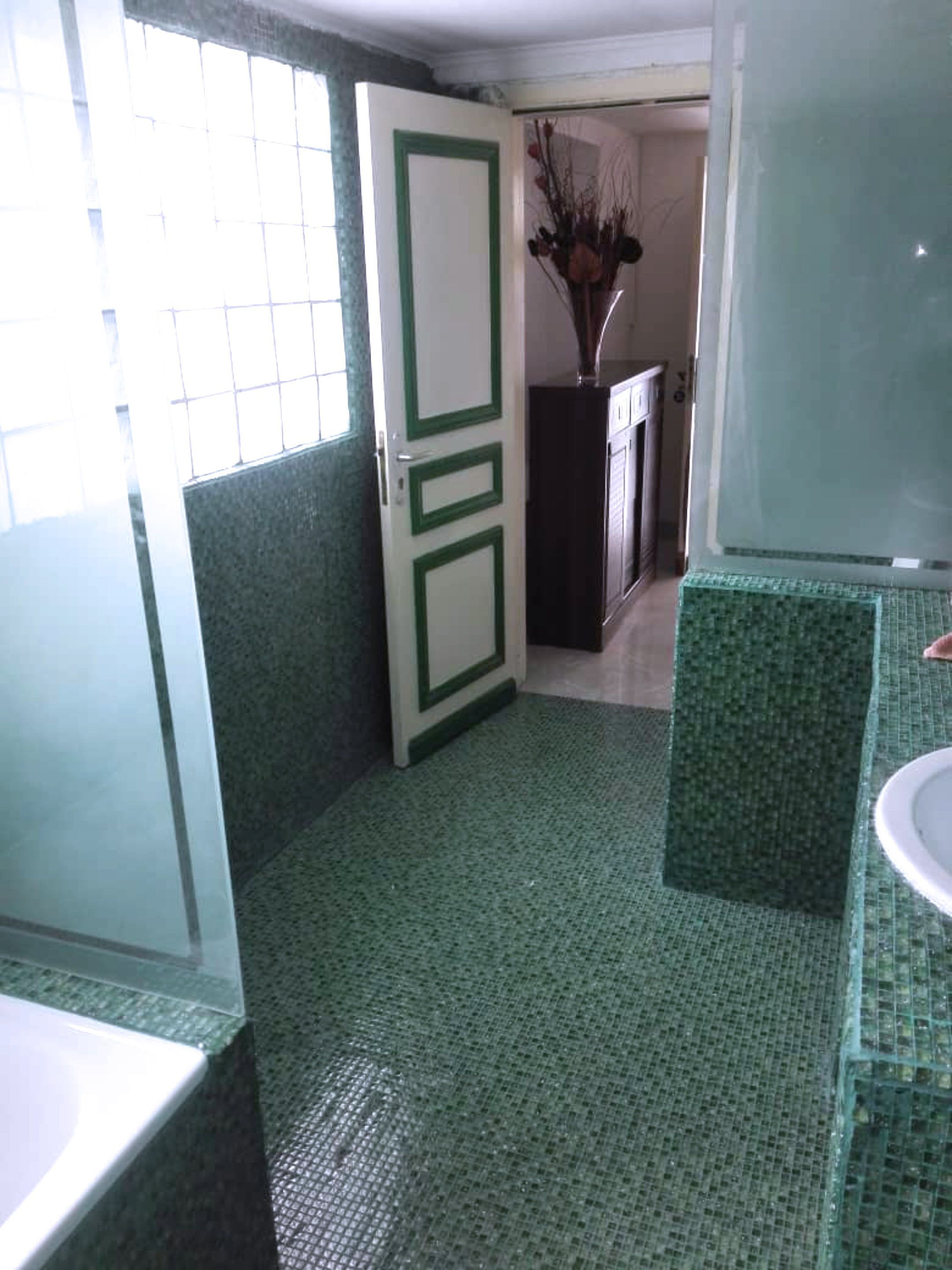 A bathroom with a green tiled floor, a white door with green trim, a white sink, and a mirror.