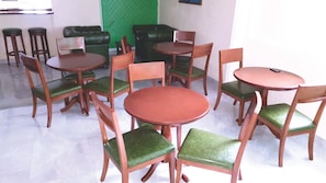 A dining area with multiple wooden tables and chairs, a green cushioned sofa, and a green textured wall. - Le Patio (Libreville)