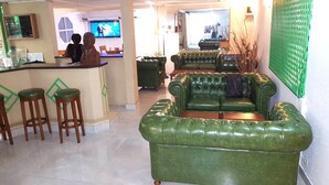 Una zona de bar con taburetes, un sofá verde y una pantalla de televisión al fondo.