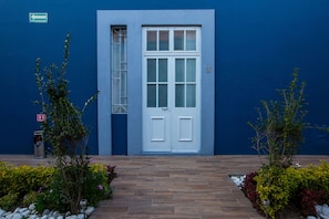 A blue building with a white door, a fire exit sign, and a small trash bin. - Xoxula by Inmense (San Pedro Cholula)