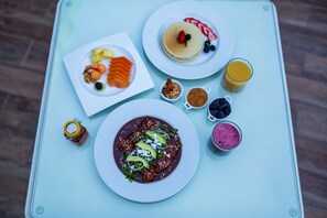 A table with a variety of breakfast items including pancakes, a fruit plate, a bowl of soup, and a glass of orange juice.
