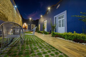 A courtyard with a wooden pathway, metal chairs, and a blue building with a door marked '3'.