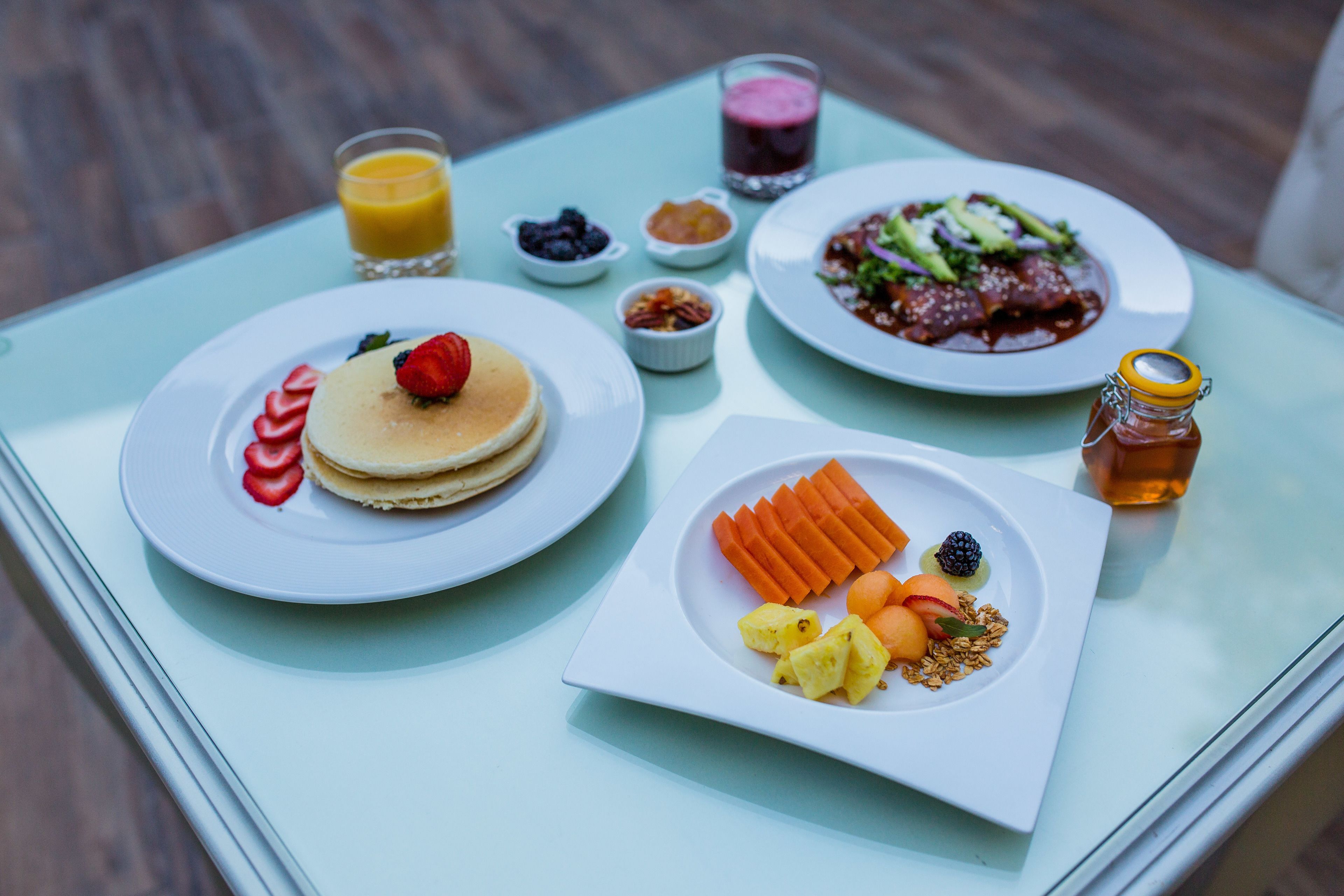 A breakfast table with pancakes, fruit, a salad, and a glass of juice.