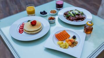 A breakfast table with pancakes, fruit, a salad, and a glass of juice.