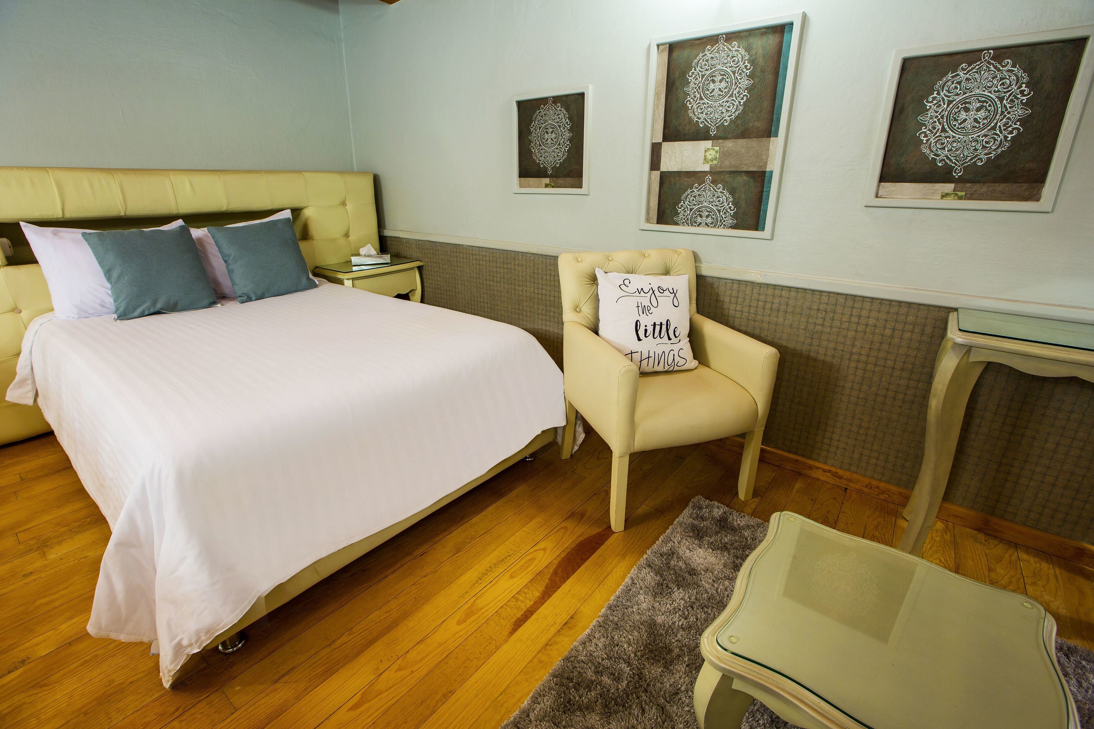 Un dormitorio con una cama, una silla con un cojín, una mesita de noche y una pequeña mesa.
