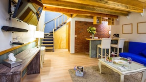 Un vaste espace de vie doté d’un plafond en bois, d’un canapé bleu, d’une table à manger où est dressé un repas, et d’un escalier menant à un niveau supérieur.