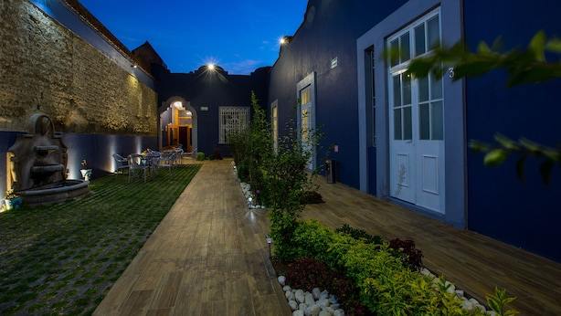 Un patio con muro de piedra, camino de madera y zona de estar con sillas y una mesa.