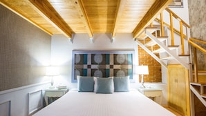 Une chambre avec un grand lit, un plafond en bois, un mur en briques et un escalier.