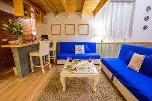 A living room with a blue sofa, a small dining table with food and drinks, a white chair, and a brick wall. - Xoxula by Inmense (San Pedro Cholula)