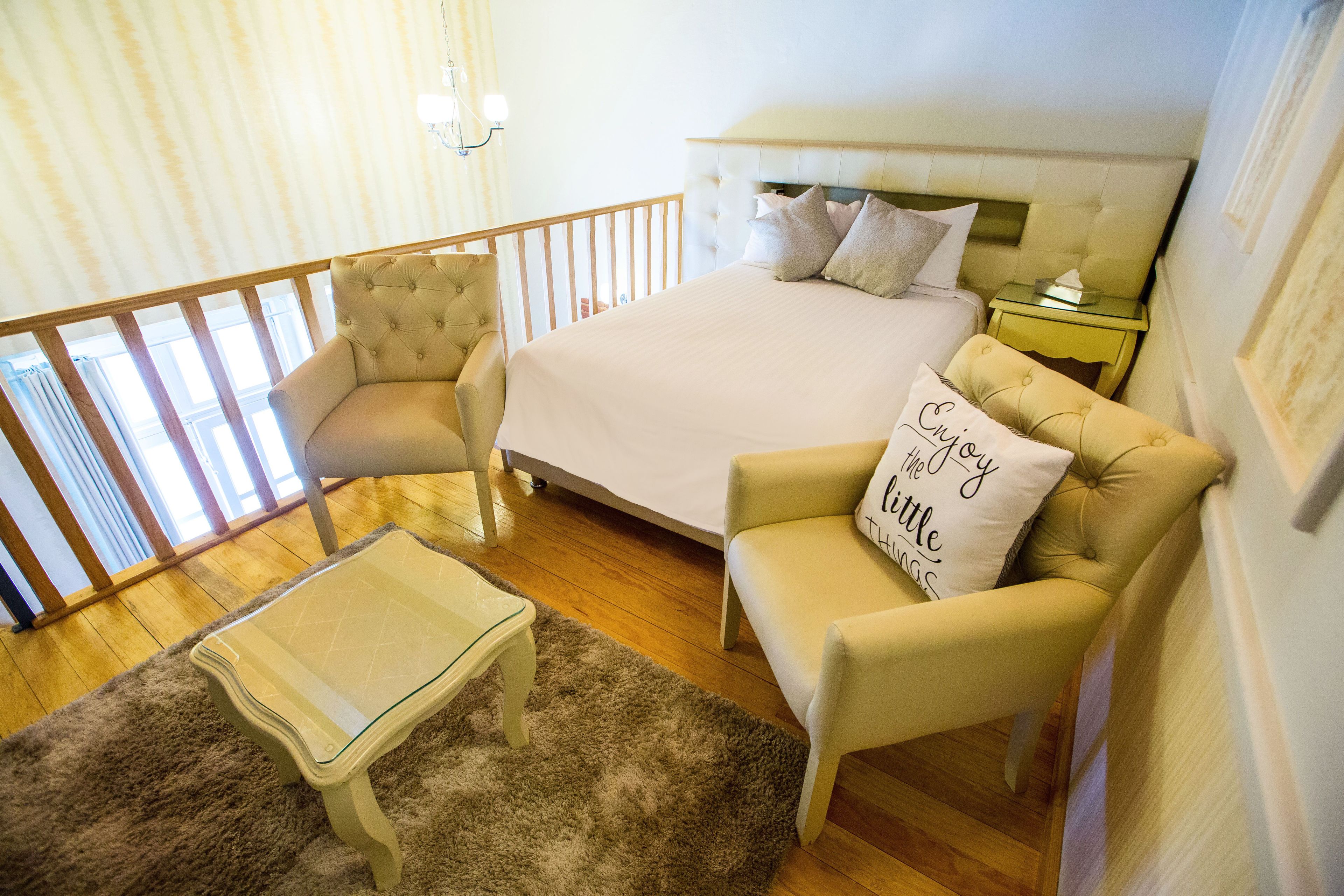 Un dormitorio con una cama, dos sillones, una mesita de centro de cristal y una mesita de noche.