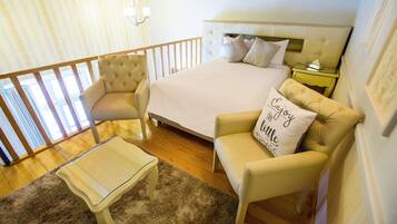 Un dormitorio con una cama, dos sillones, una mesita de centro de cristal y una mesita de noche.
