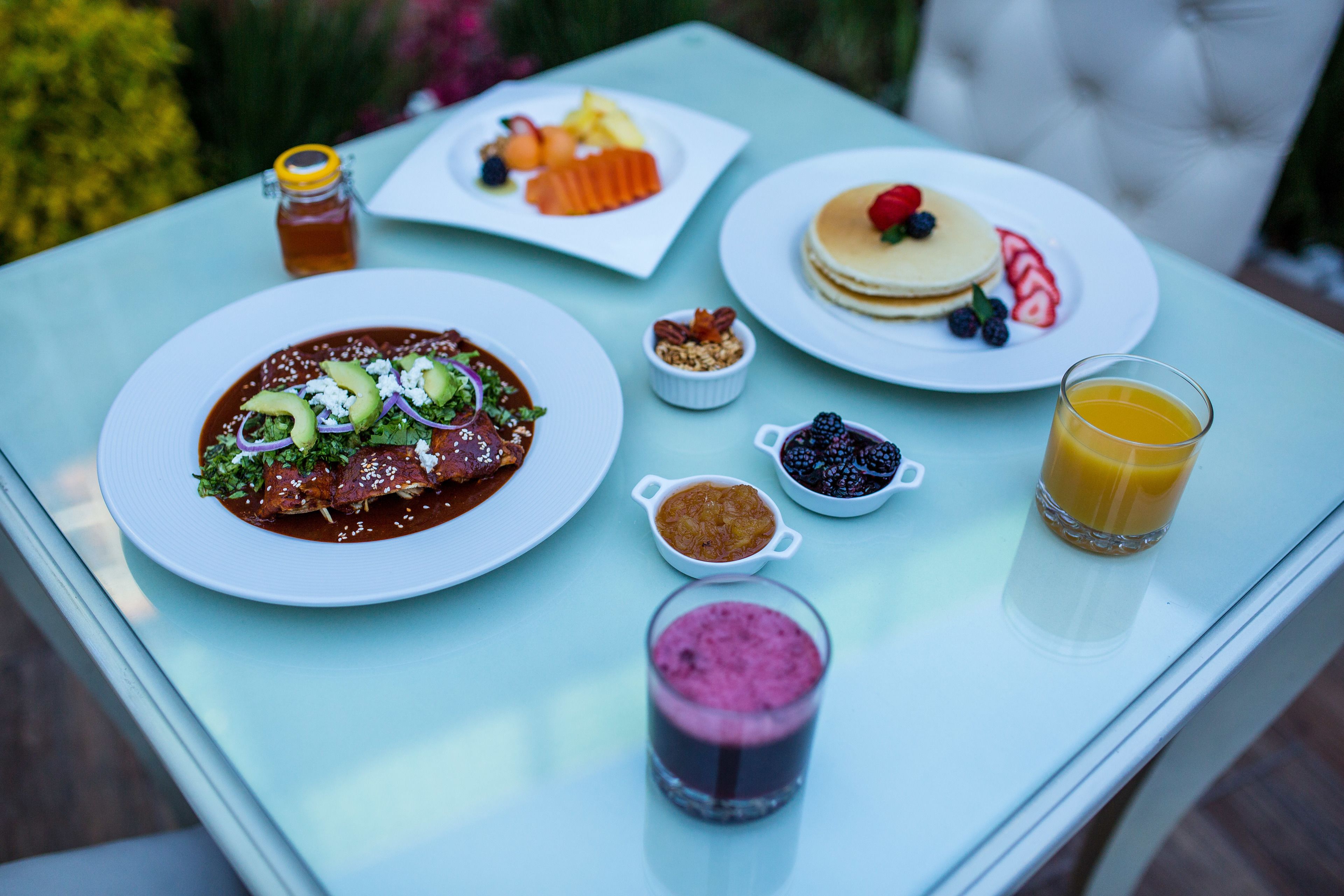 A table with various breakfast items including pancakes, a fruit plate, a bowl of soup, and a glass of orange juice.