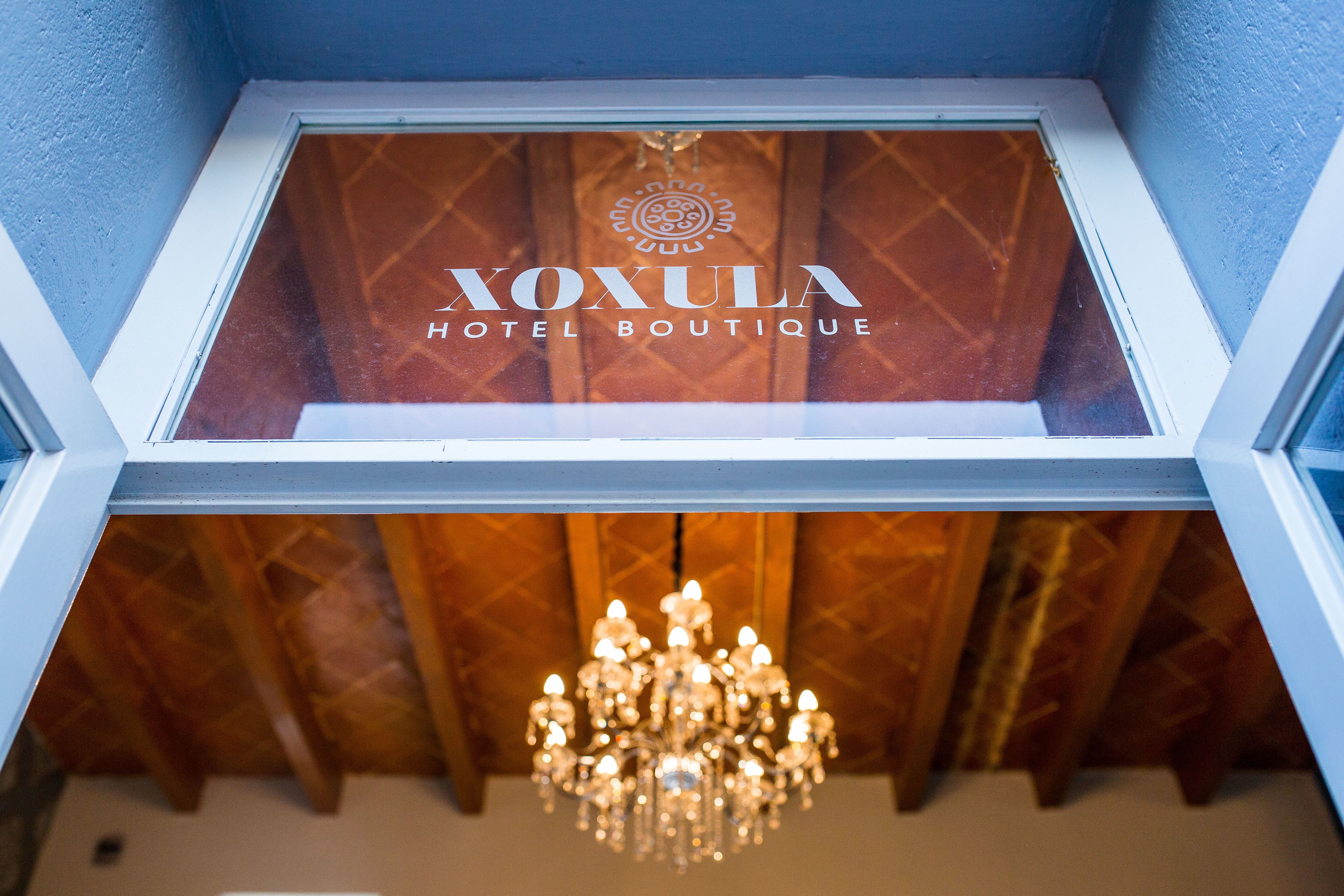 A hotel window with the name "XOXULA HOTEL BOUTIQUE" and a chandelier visible below.
