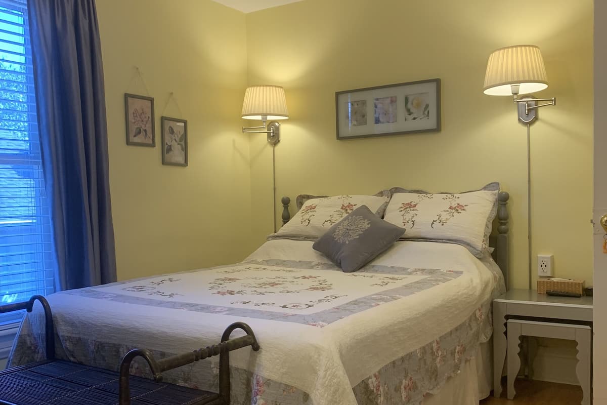 Ein Schlafzimmer mit einem Bett, zwei Nachttischlampen, einem Sessel und einem Fenster mit Vorhängen.